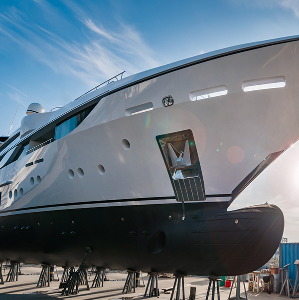 Wide shot of the bow of a new  white modern superyacht on dry dock, with a bulbous bow on a sunny day, with stainless steel  anchor on a sunny day with blue sky